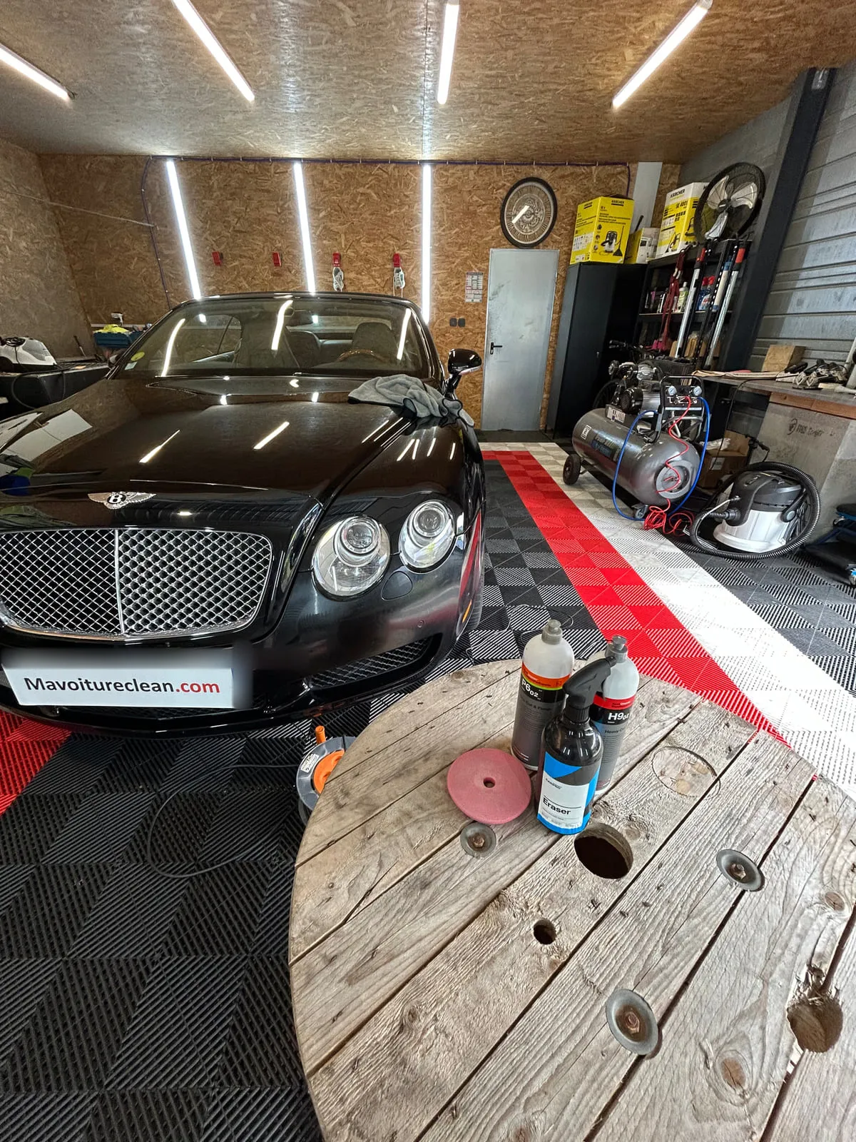 Bentley noire dans l'atelier éclairé, flacons et patin de polissage posés sur un touret en bois au premier plan