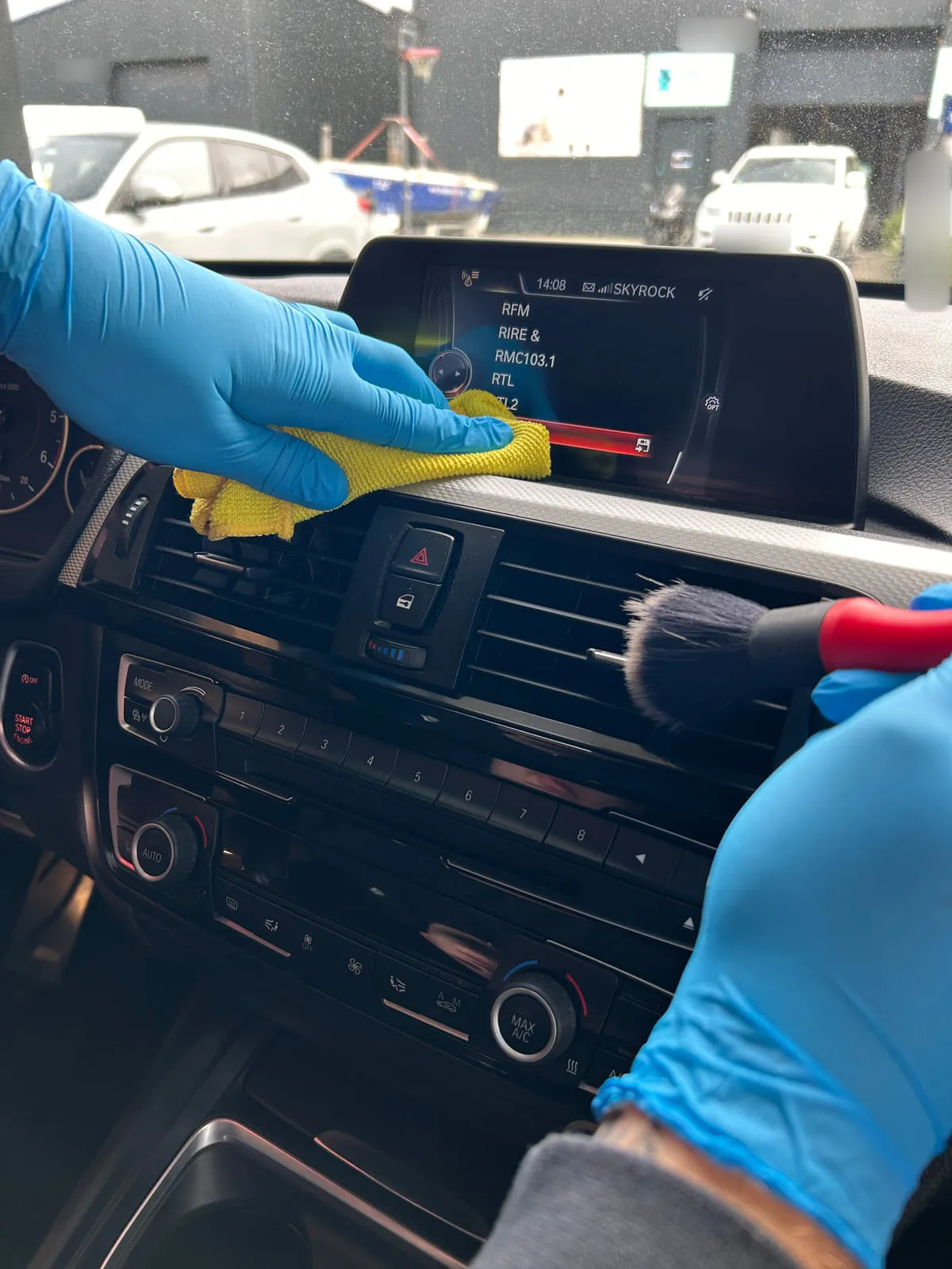 Mains gantées de bleu sur la planche de bord d'une BMW : microfibre jaune et pinceau dans les aérateurs