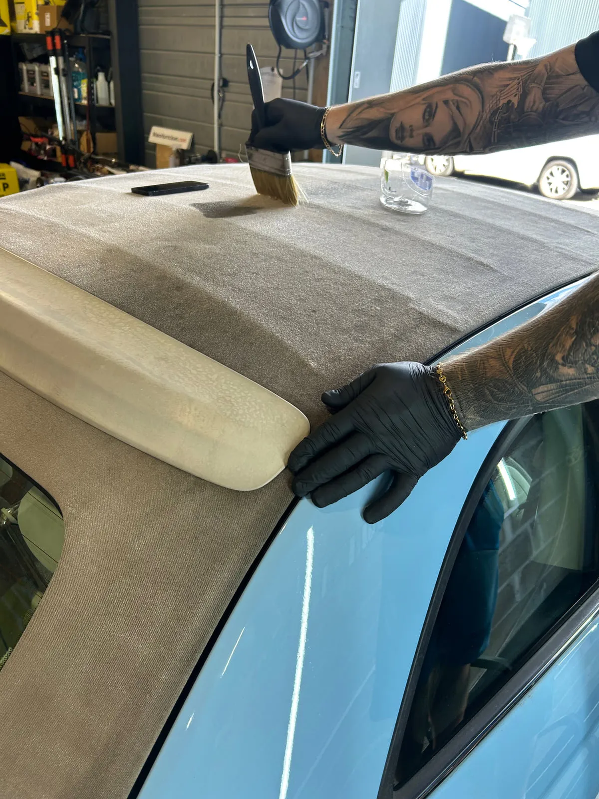 Pinceau passé sur la capote en tissu d'un cabriolet bleu clair, une main gantée de noir posée sur la carrosserie