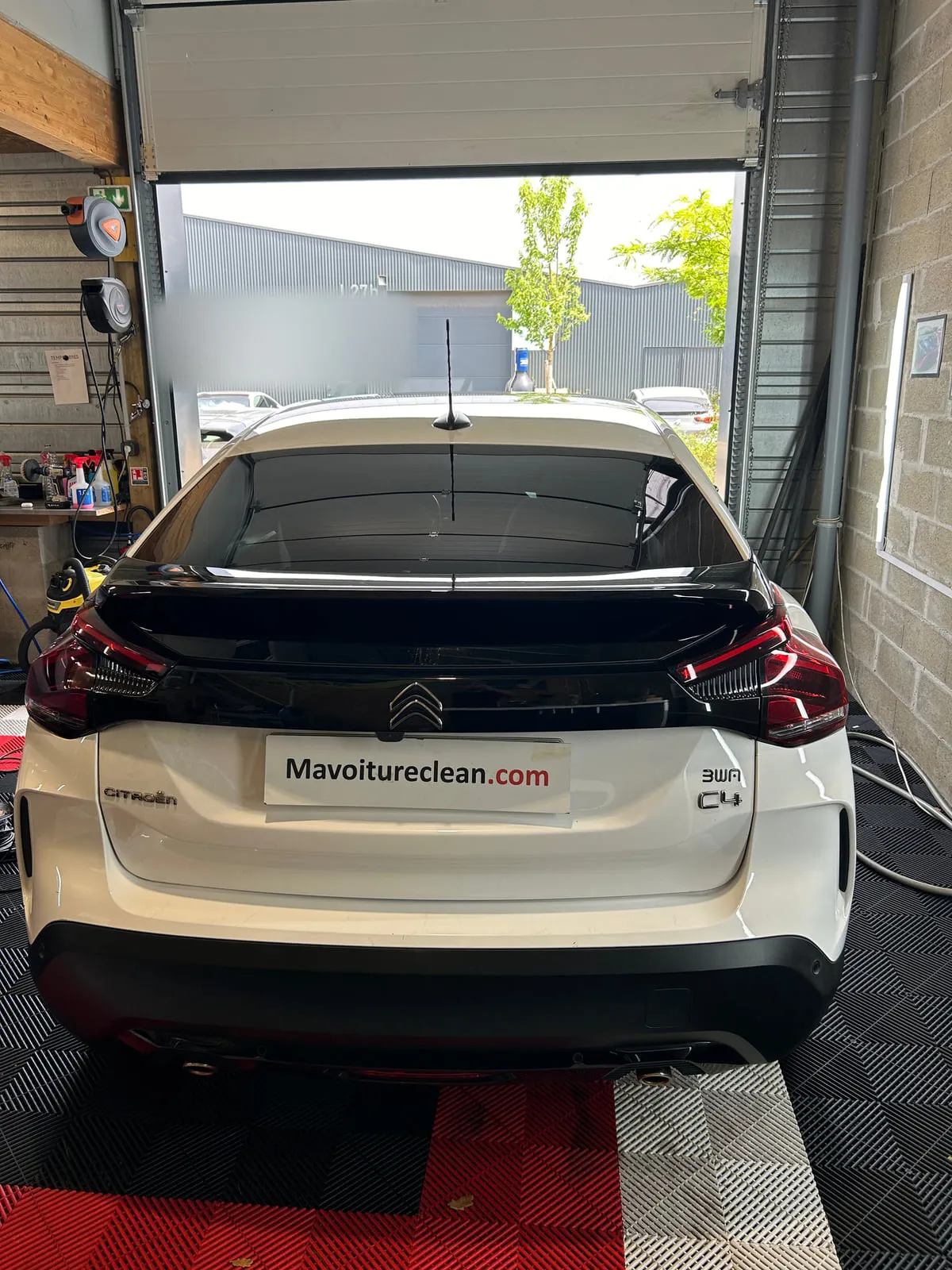 Citroën C4 blanche vue de l'arrière dans l'atelier, chevrons et badge C4 sur le hayon, porte de l'atelier ouverte