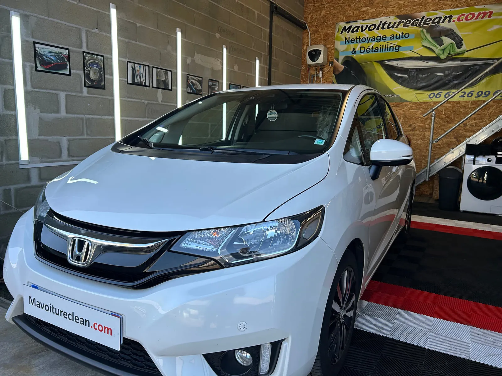 Honda blanche vue de trois quarts avant dans l'atelier, bannière Mavoitureclean.com au mur