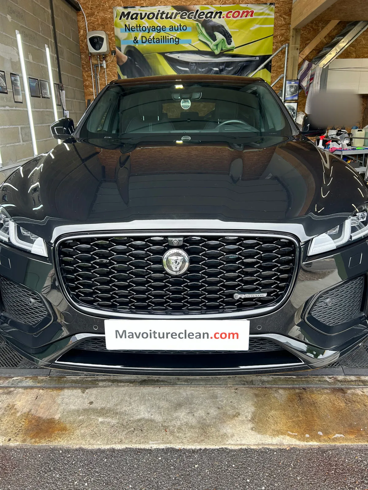 Jaguar noire vue de face dans l'atelier, calandre noire à l'emblème Jaguar, bannière Mavoitureclean.com au fond