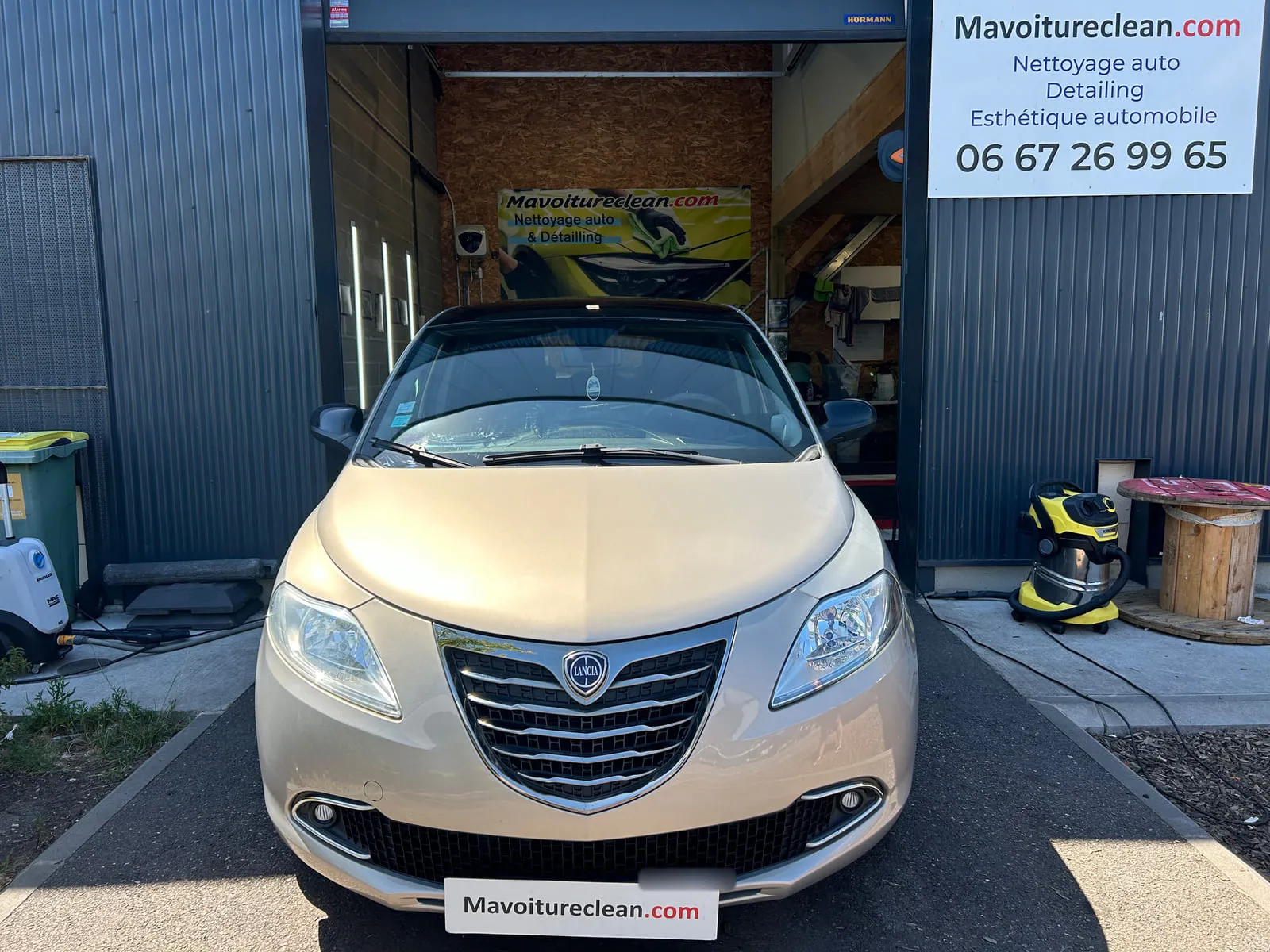 Lancia beige vue de face devant l'atelier, enseigne Mavoitureclean.com avec numéro de téléphone sur la façade