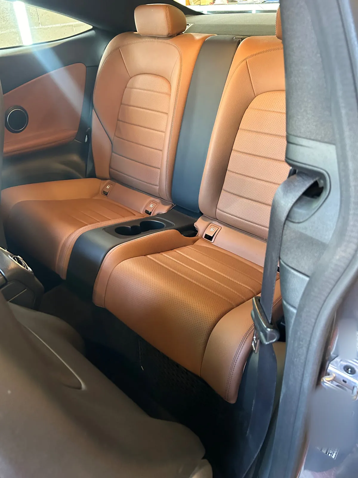 Banquette arrière en cuir cognac perforé à surpiqûres d'un coupé : deux places séparées par un accoudoir central à porte-gobelets