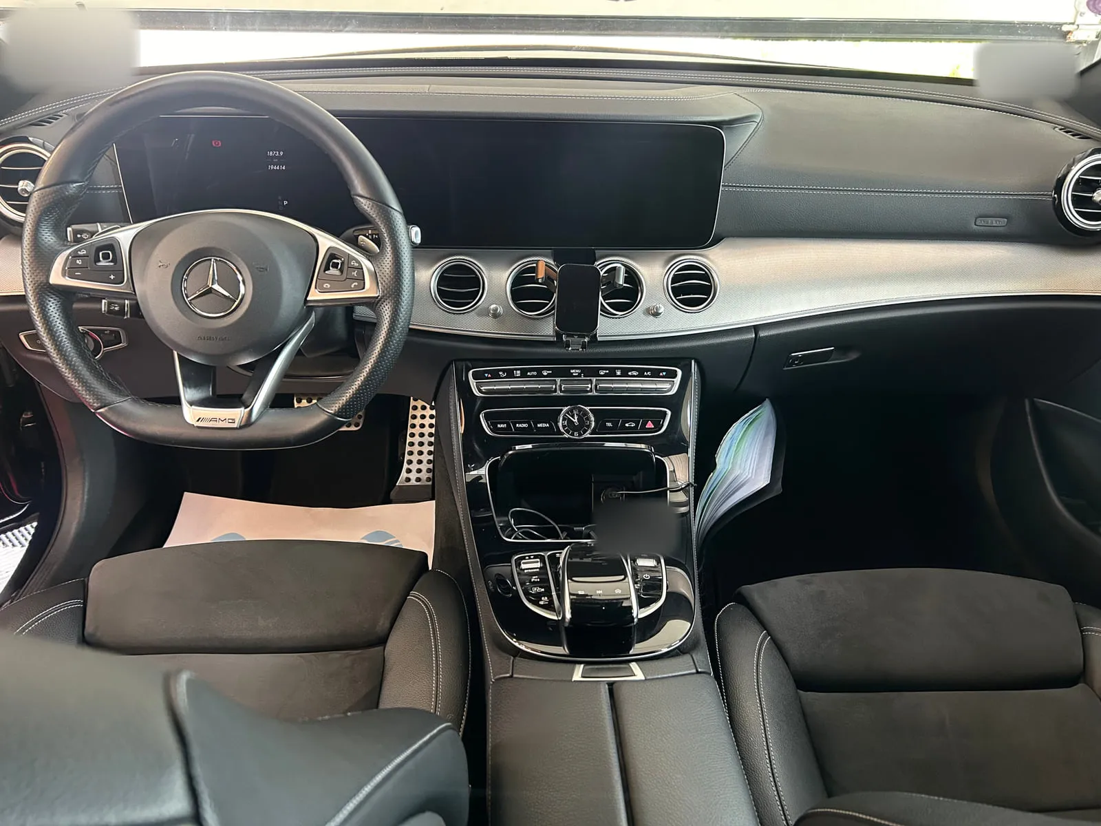 Planche de bord d'une Mercedes vue de face : double écran, volant sport à l'étoile, sièges noirs
