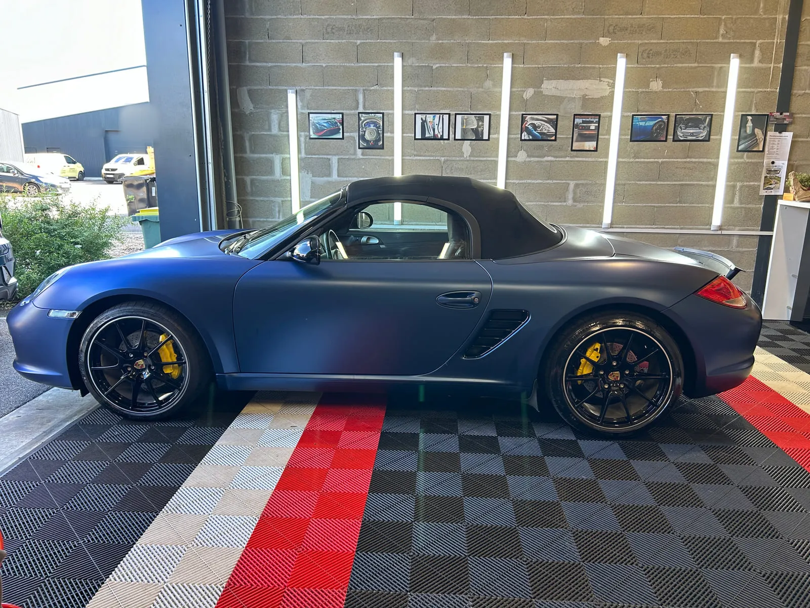 Porsche cabriolet bleu mat vue de profil, capote noire fermée, jantes noires et étriers jaunes, dans l'atelier