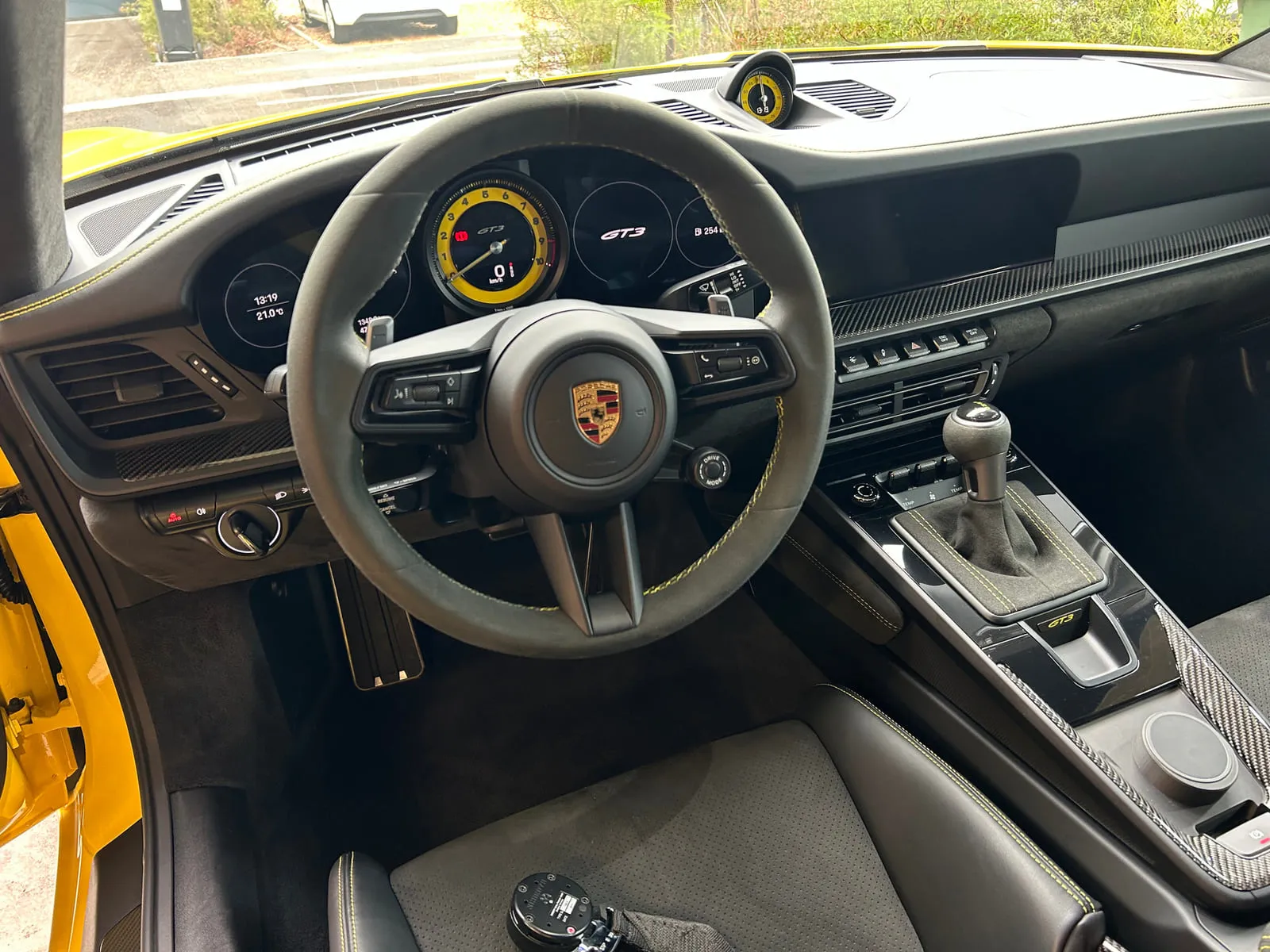 Poste de conduite d'une Porsche GT3 : volant à garniture façon daim aux surpiqûres jaunes, compteur central jaune, inscription GT3 sur l'écran et sur la console, levier de vitesses à soufflet, éléments en carbone