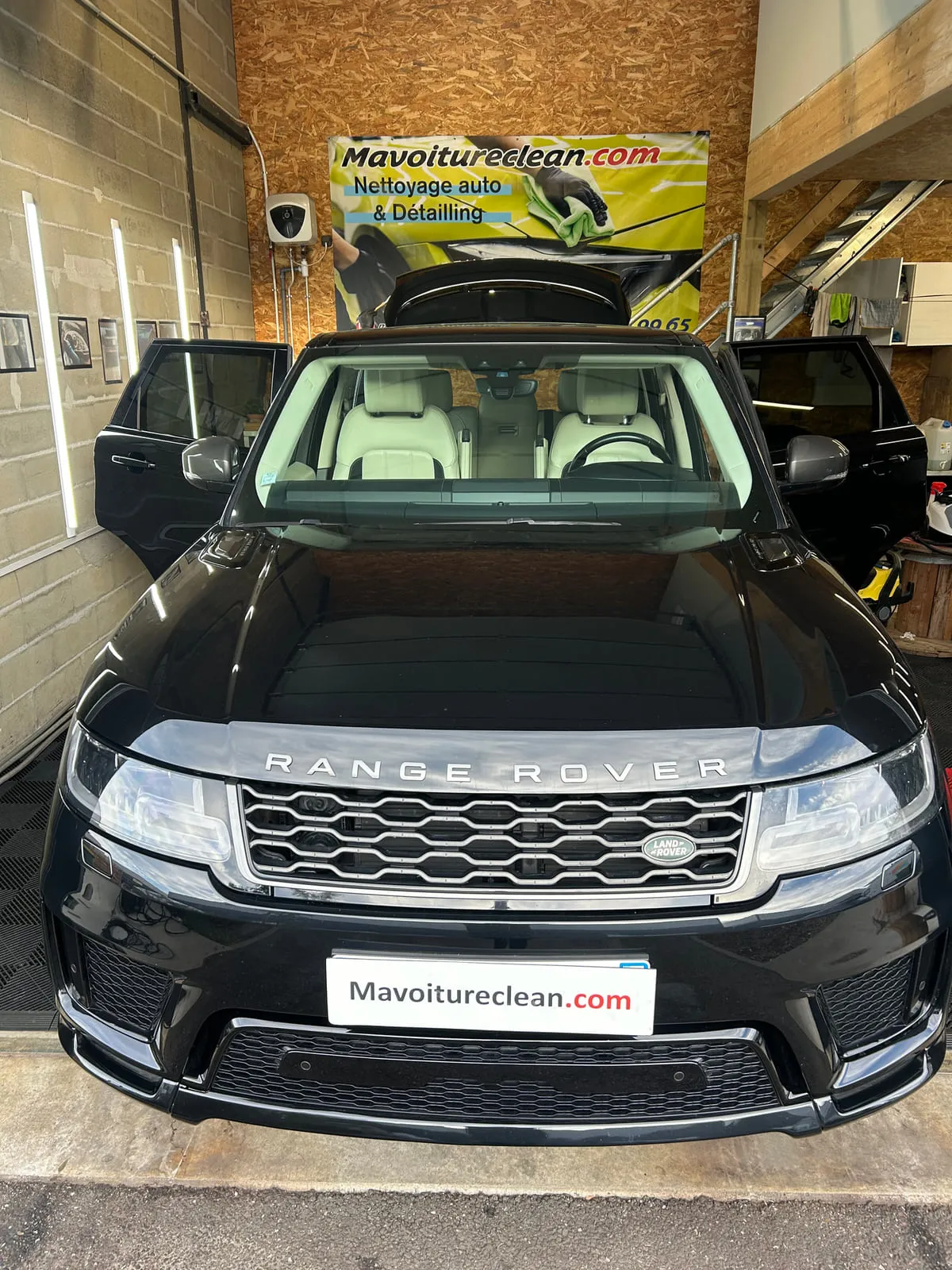 Range Rover noire vue de face dans l'atelier, portes arrière ouvertes sur une sellerie claire, bannière Mavoitureclean.com au fond
