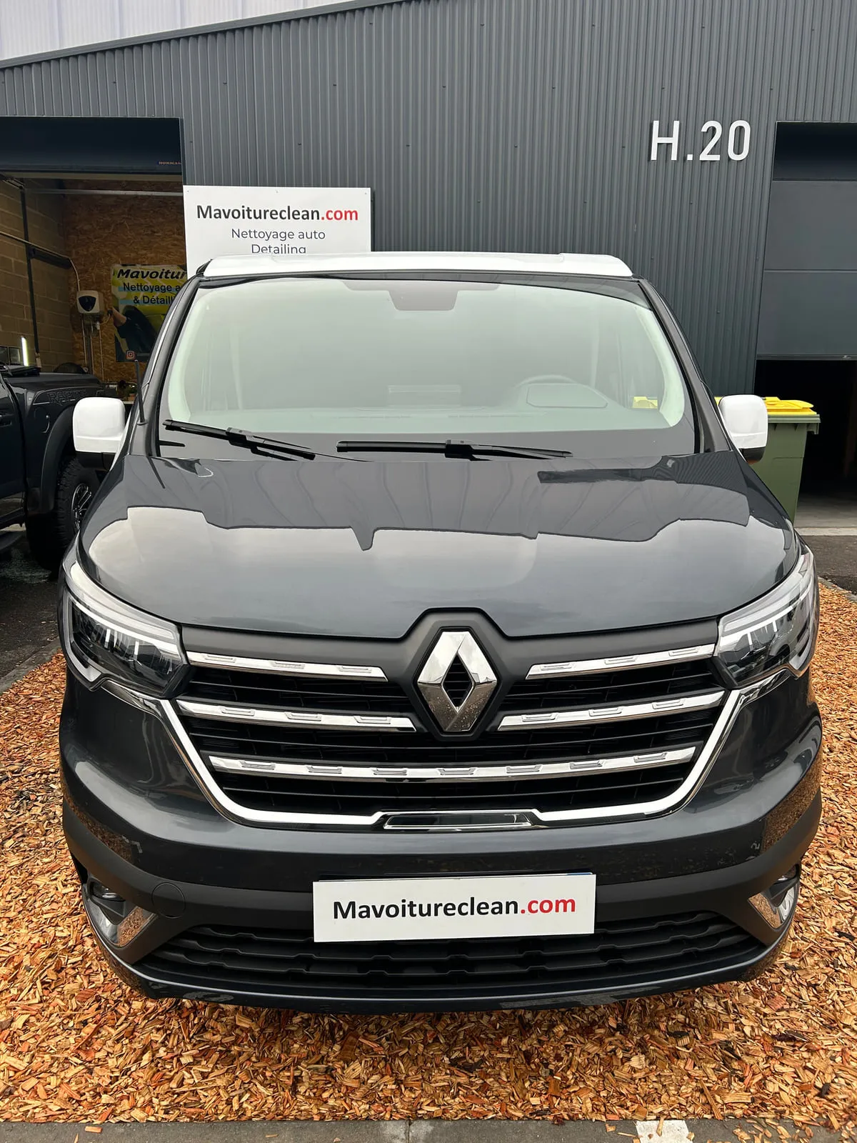 Fourgon Renault gris anthracite vu de face : calandre noire à baguettes chromées, losange Renault, panneau Mavoitureclean.com à la place de la plaque