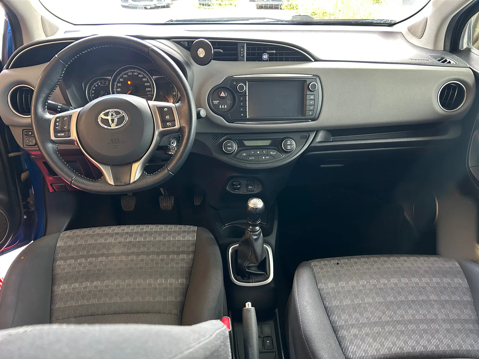 Planche de bord d'une Toyota vue de face : volant au logo Toyota, écran central, sièges en tissu gris